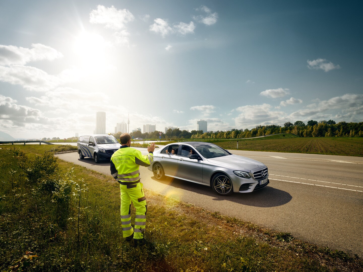 Mercedes-Benz Service24h | Mercedes-Benz Un técnico del servicio posventa de Mercedes-Benz hace señales desde el margen de la calzada a un niño sentado en un Mercedes que se aproxima al lugar.